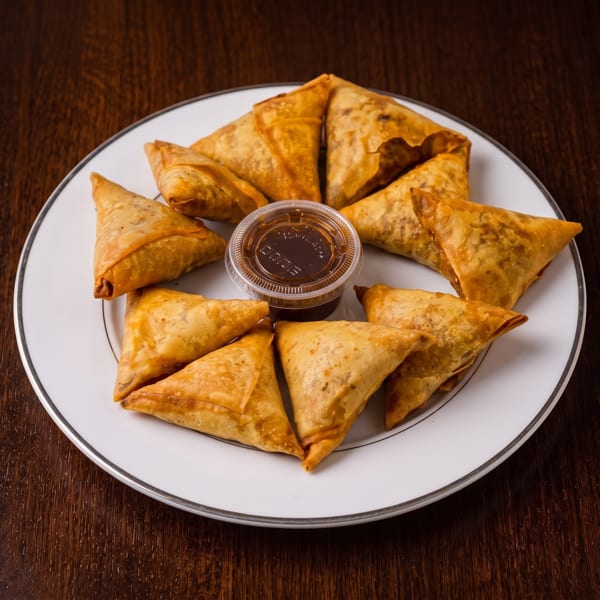Golden-brown samosas arranged on a white plate with a small container of dipping sauce.