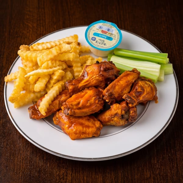 A plate of buffalo wings, crinkle-cut fries, celery sticks, and a ranch dressing cup.