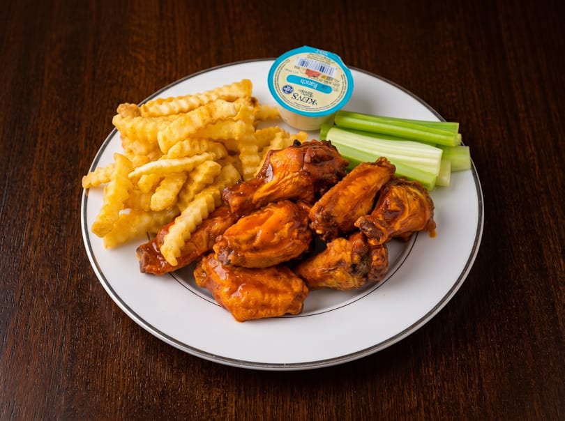 A plate of buffalo wings, crinkle-cut fries, celery sticks, and a ranch dressing cup.