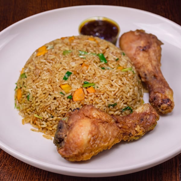 Fried rice with carrots and green onions, two fried chicken drumsticks, and a side of sauce.