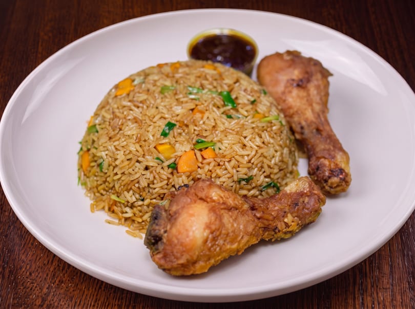 Fried rice with carrots and green onions, two fried chicken drumsticks, and a side of sauce.