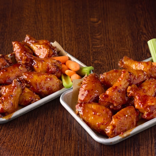 Two trays of glazed chicken wings with baby carrots, celery sticks, and ranch dressing.