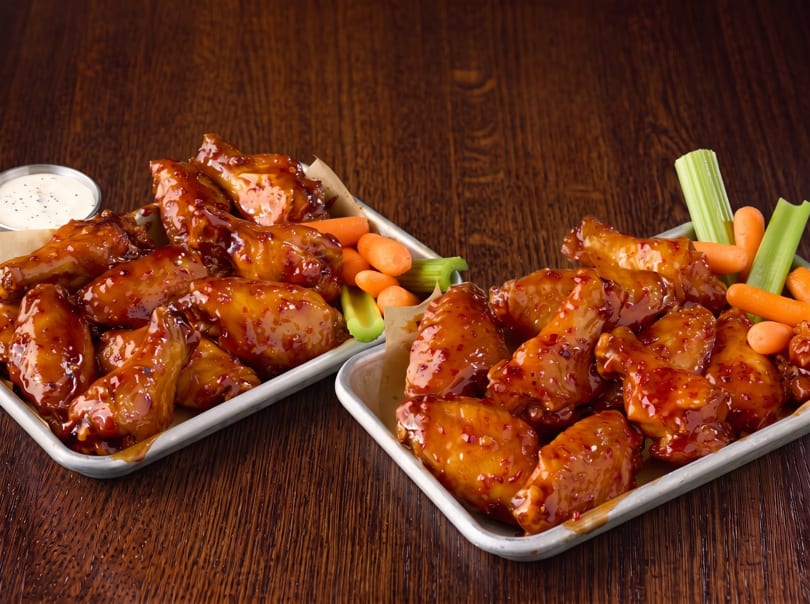 Two trays of glazed chicken wings with baby carrots, celery sticks, and ranch dressing.