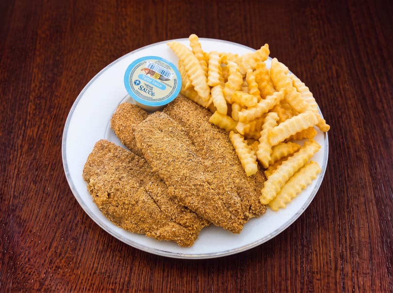 A white plate with three breaded fish fillets, crinkle-cut fries, and a cup of tartar sauce.