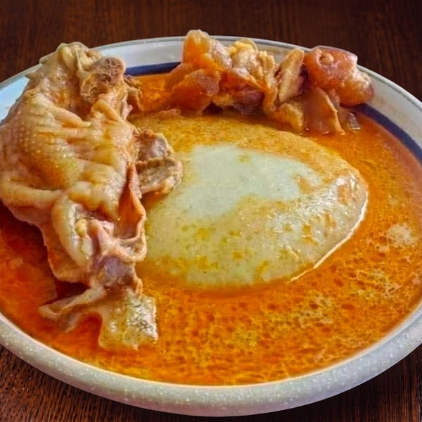 A plate of fufu and chicken in a rich orange soup on a wooden table.