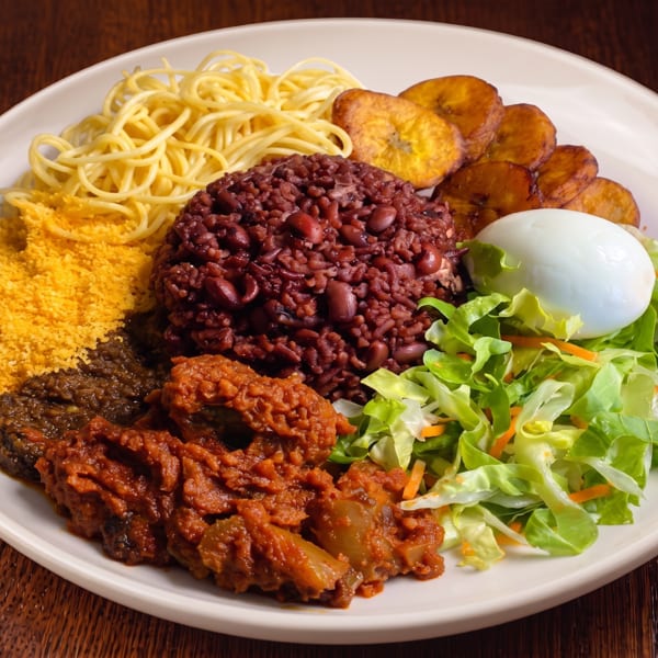 A large plate of food with rice and beans, spaghetti, plantains, salad, and meat.